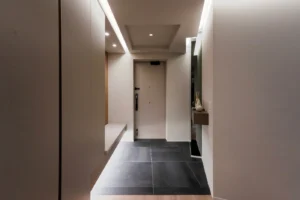 After - 鋭角な壁に配したミラーと飾り棚、ルーバー一体型のベンチ、天井の間接照明が、機能性と奥行きのある品格を両立させた玄関